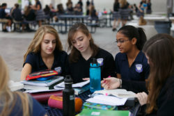 Students gather around a table and all read from a paper
